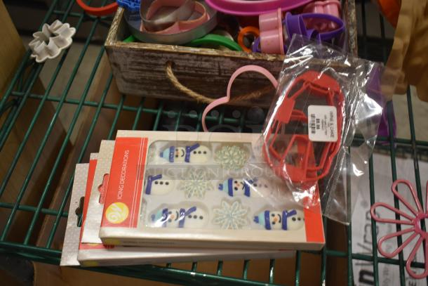 Box of Wilton icing decorations with snowman and snowflake designs, alongside assorted cookie cutters in a wooden tray.