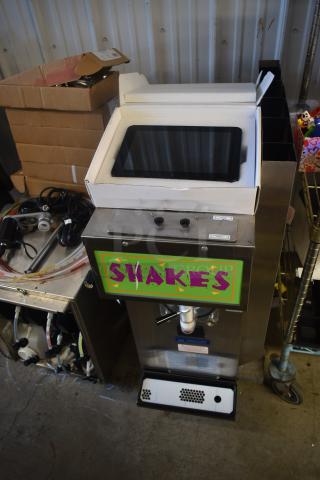 Commercial milkshake machine with colorful "SHAKES" sign, monitor screen, and buttons. Brand: Taylor. Some components disassembled nearby.