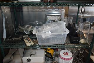 A wire shelf with assorted kitchen items includes a plastic container, blender base, glass jars, and spiral whisk. Some items packaged, labeled "Qty".