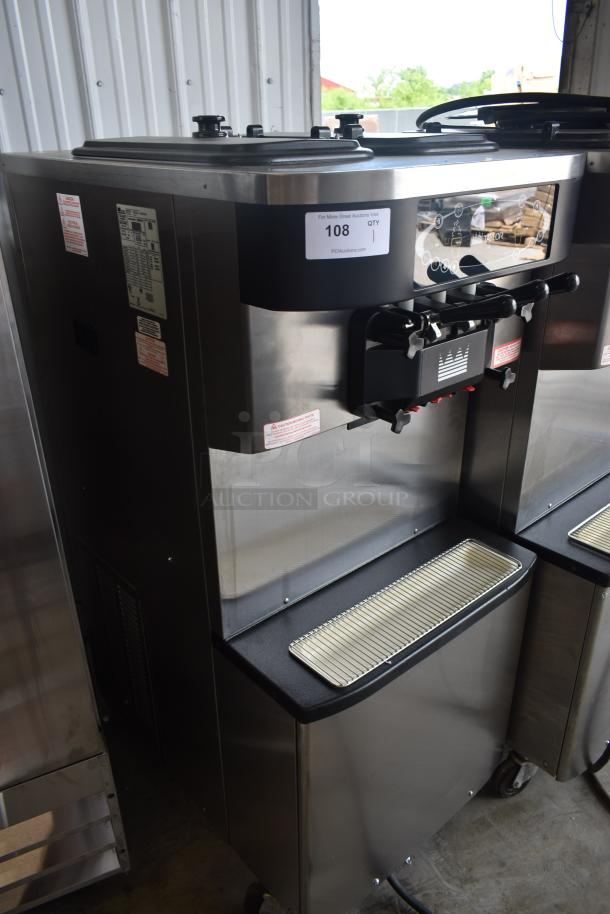 Commercial soft serve machine in stainless steel, features dual hoppers and levers. Label reads "108." Good condition.