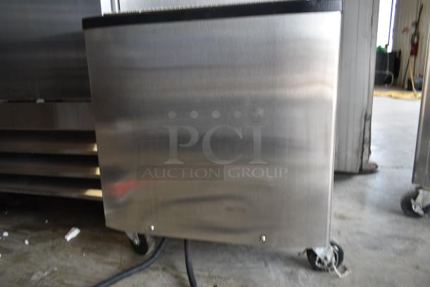 Industrial stainless steel appliance on wheels, showing some wear. No visible labels or markings. Potentially a commercial cooler or heater.