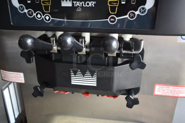 Taylor commercial ice cream machine, stainless steel, multiple dispensers, control panel with icons, caution labels visible.