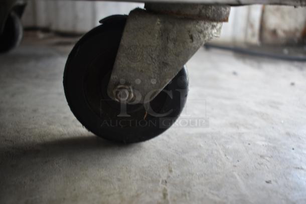 Metal caster wheel on concrete floor, slightly worn with visible rust and markings. Suitable for industrial equipment.