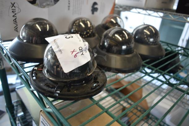 Six Avamix dome cameras on a metal shelf, marked with a tag indicating quantity. Cameras appear used.