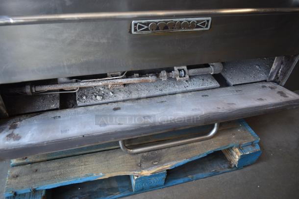 Commercial pizza oven by Attias, stainless steel, shows signs of wear and dust, visible piping, placed on wooden pallet.