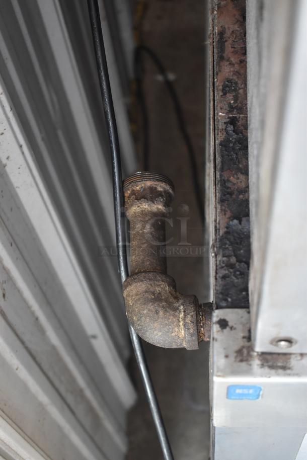 Rusty metal pipe attached to an industrial surface, showing visible wear. Nearby, an NSF-certified label is partially visible.