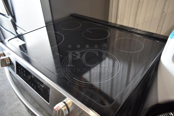 Stainless steel electric range with glass cooktop, four burners, and digital control panel. Light wear, tag marked "119".