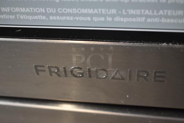 Frigidaire stainless steel appliance with engraved logo, showing a brushed finish. Manufacturer's label indicates anti-tip bracket advice in French.