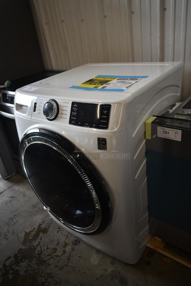 White front-load washing machine with digital controls, chrome accents, and energy efficiency sticker. Appears in excellent condition.