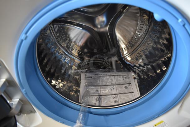 Front-loading washing machine interior with stainless steel drum, blue rim, and installation guide. Brand-new condition.