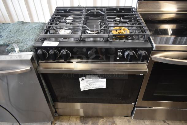 Samsung stainless steel gas range with four burners, including a gold-colored burner. Push-to-turn knobs. Warning label visible.