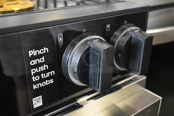 Close-up of two black stove knobs with markings for adjustment. Label reads "Pinch and push to turn knobs."
