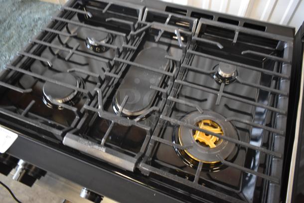 Black gas stove with four burners and metal grates. Features a central elongated burner. Condition appears excellent.
