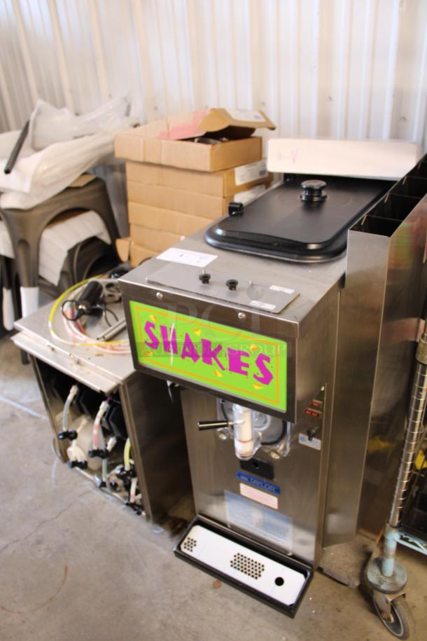 Commercial shake machine with "SHAKES" label, stainless steel body, model by Taylor, used condition, visible pipes and controls.