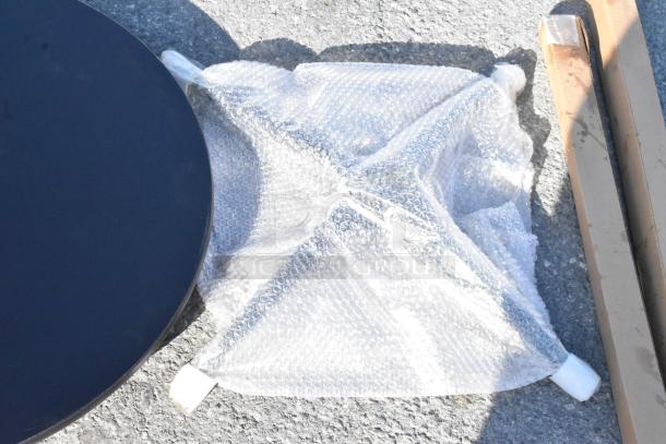 Black circular tabletop partially wrapped in bubble wrap on a concrete surface. Nearby cardboard packaging.