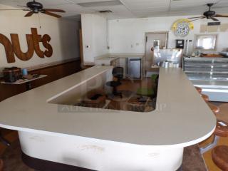 Vintage diner counter with light grey laminate countertop, brown bar stools, and a retro "Spudnuts" wall clock. Fair condition.