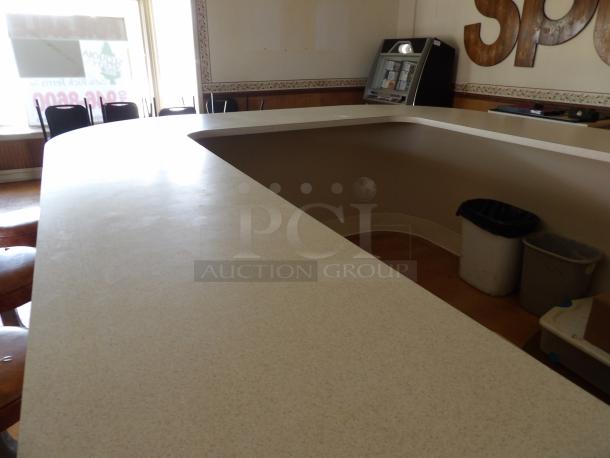 Large L-shaped bar counter in good condition, neutral-colored surface, equipped with stools and adjacent to a jukebox.