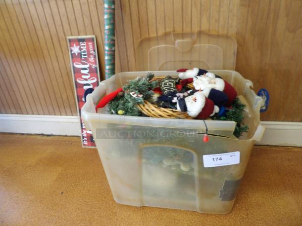 Plastic bin filled with Christmas decorations, including Santa figures and greenery, labeled "174."