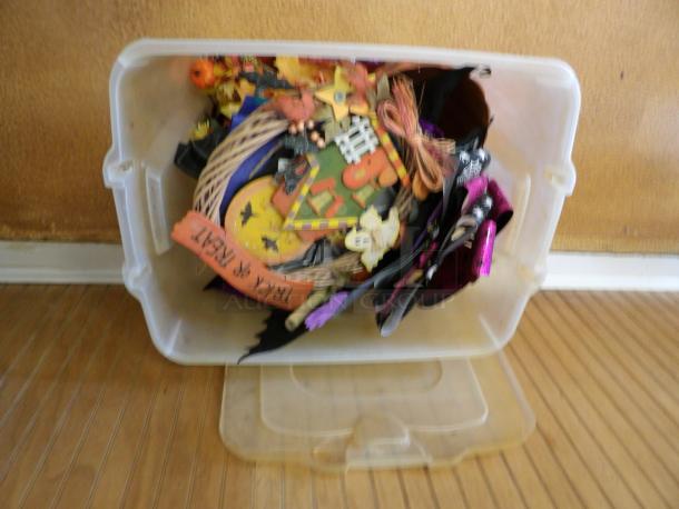 Plastic bin filled with assorted Halloween decorations, including pumpkins, bats, and "Trick or Treat" sign.