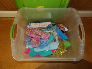 Plastic bin filled with assorted colorful paper flip-flops, craft materials, and small decorative items.
