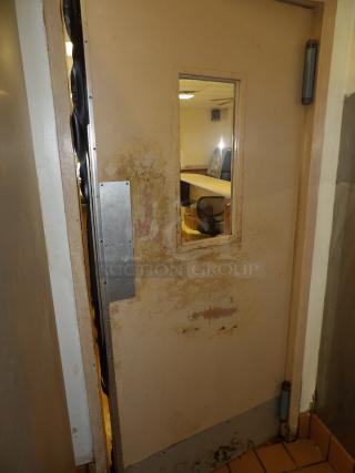 Worn industrial door with rectangular window, showing peeling paint and signs of heavy use. Interior view includes office furniture.