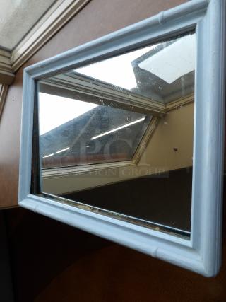 Rectangular mirror with light blue wooden frame, showing slight wear. Reflecting a roof skylight, showcasing character.