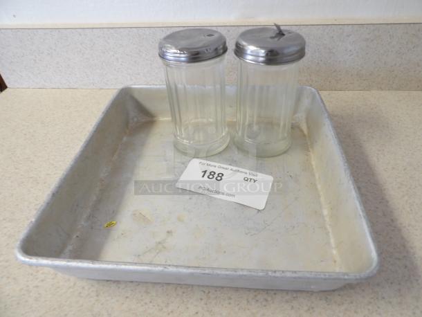 Aluminum baking tray with two clear glass shakers, metal lids, auction tag numbered 188. Tray shows wear.