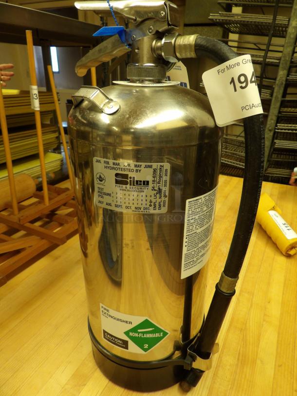 Stainless steel fire extinguisher, model Silco, hydro-tested, non-flammable rating. Auction tag 194 visible.