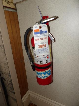 Red fire extinguisher with "Silco Fire & Security" tag, serviced for 2024. Suitable for all fire types, includes usage instructions.