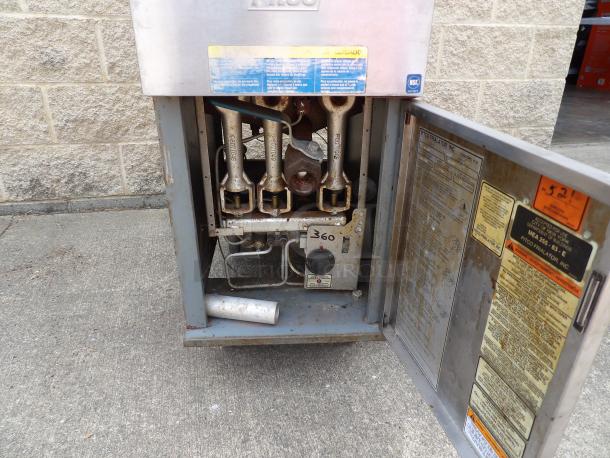 Industrial gas fryer with open compartment, showing internal components. Visible labels indicate safety instructions and model details. Slight rust present, suggesting wear.