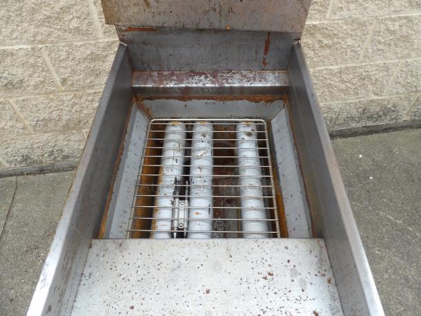Commercial outdoor grill in used condition with visible rust and grease. Features metal grates and burner tubes.