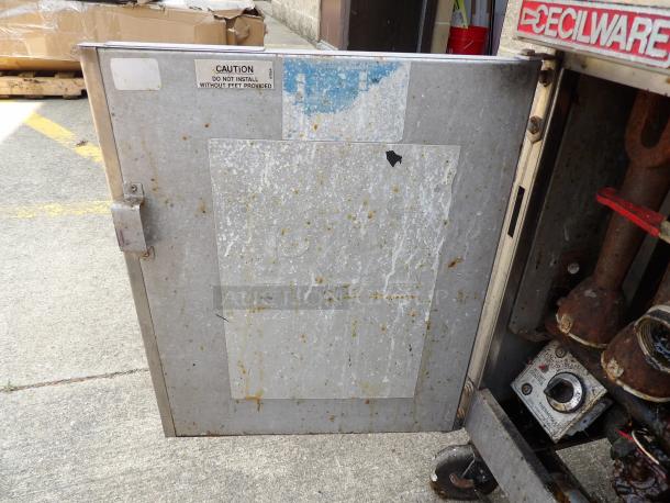 Metal Decilware kitchen appliance door, showing wear and grime, hinged with caution label warning against installation without feet.