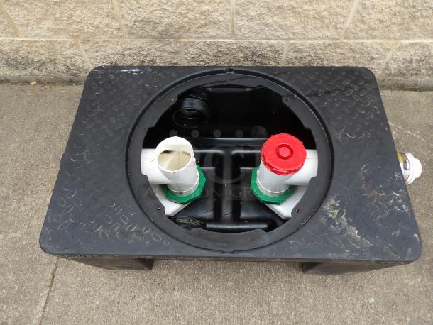 Black plastic tank with circular opening, two white PVC pipes, and one red cap. Surface shows wear.