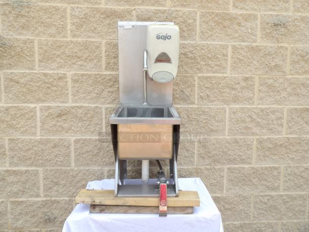 Stainless steel hand wash sink with Gojo soap dispenser, mounted on wooden platform. Good condition, ideal for commercial use.