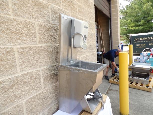 Stainless steel commercial handwashing sink with foot pedal, Gojo soap dispenser, mounted on brick wall. Good condition.