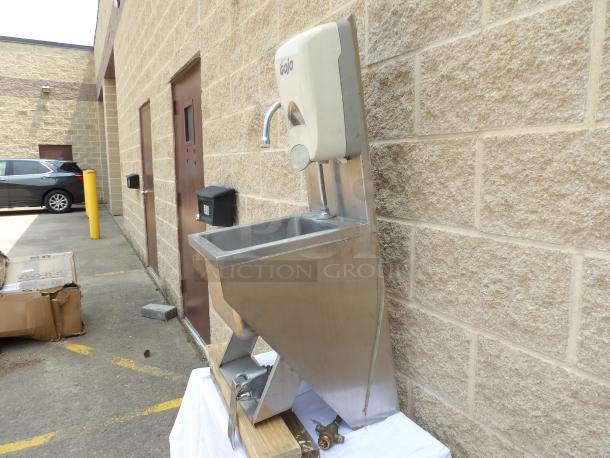 Stainless steel wall-mounted hand sink with Gojo automatic soap dispenser, in good condition, set externally.