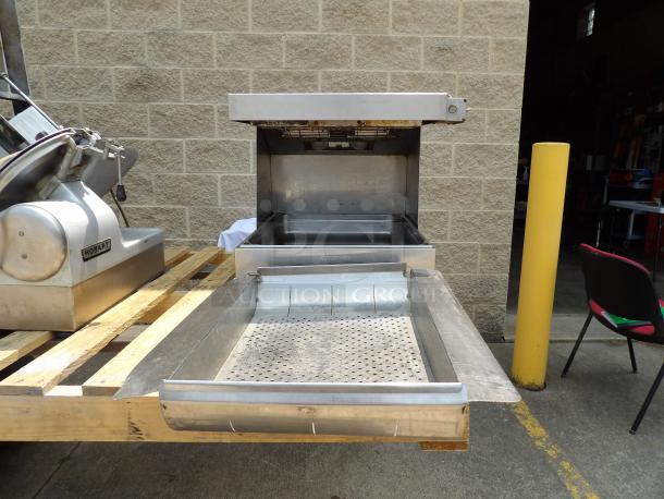 Commercial conveyor toaster with stainless steel body on a wooden pallet, showing large feed tray and heating chamber. Note: some rust on top edge.