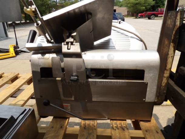 Commercial meat slicer, metal body, used condition, featuring adjustable blade and safety guard, sitting on wood pallet.