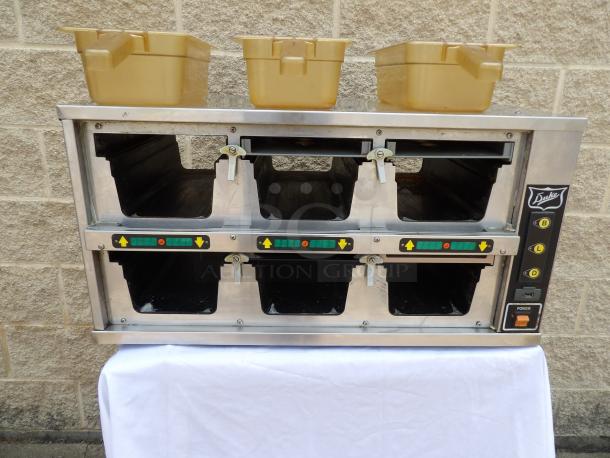 Duke warming tray with four compartments, adjustable controls, stainless steel finish, and visible power button. Includes three beige trays on top.