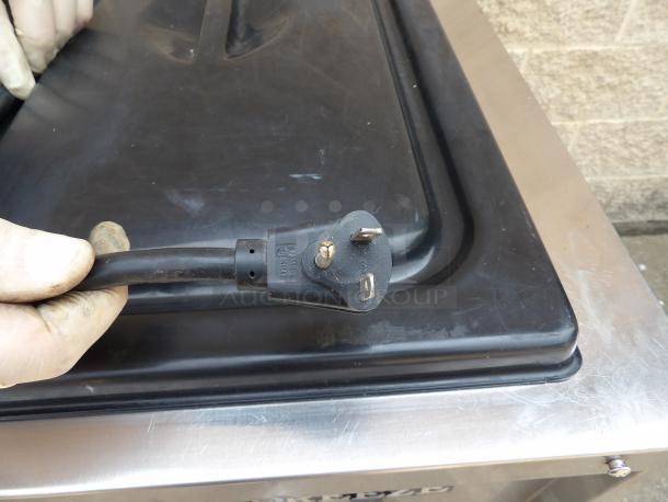 Close-up of a three-prong electrical plug with visible grounding pin. Plug shows light wear, held by gloved hand.