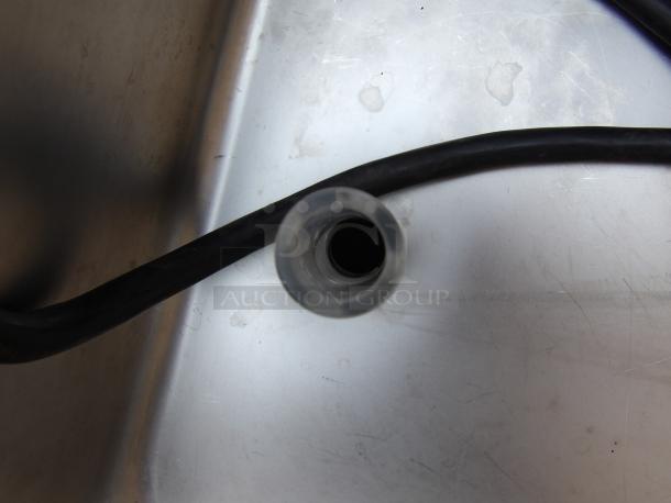Close-up of a transparent plastic tube with a black cable on a metallic surface. Appears in good condition.