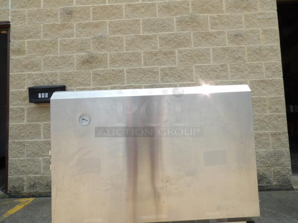 Stainless steel enclosure with a gauge, showing signs of wear. Brick wall and a mailbox labeled "148" are in the background.
