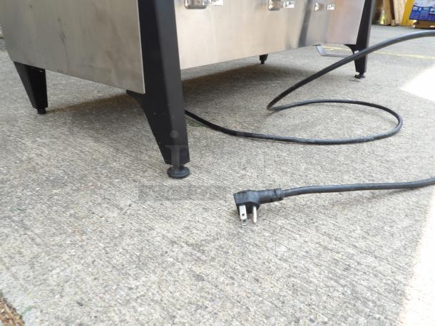 Stainless steel appliance with black legs and power cord on concrete surface. Three-prong plug visible, good condition.
