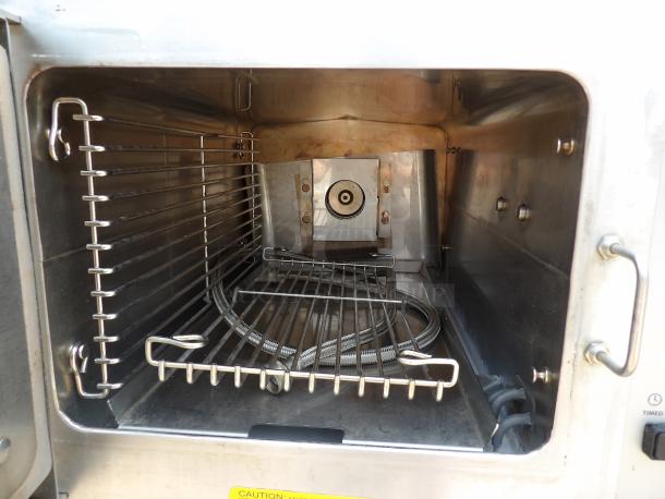 Commercial stainless steel oven interior with racks and heating element, showing minor wear. Visible caution label on the door.