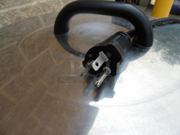 Black electrical power plug with three prongs, showing minimal wear, placed on a reflective metal surface.