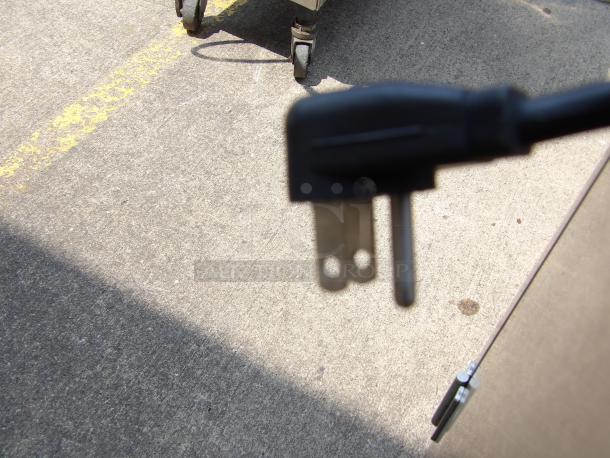 Close-up of a two-prong electrical plug with a black casing, resting on a concrete surface, showing slight wear.
