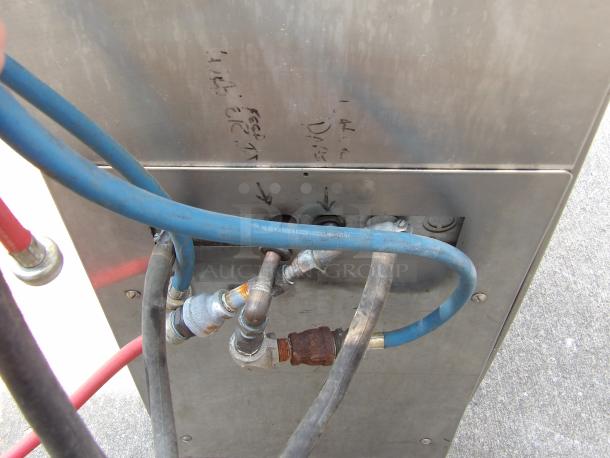 Metal panel with blue and red industrial hoses and fittings connected. Surface shows handwritten marker notations.