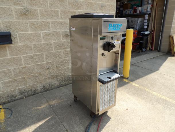 Stainless steel Electro Freeze soft serve machine on wheels, used condition, with dispensing lever and branding visible.