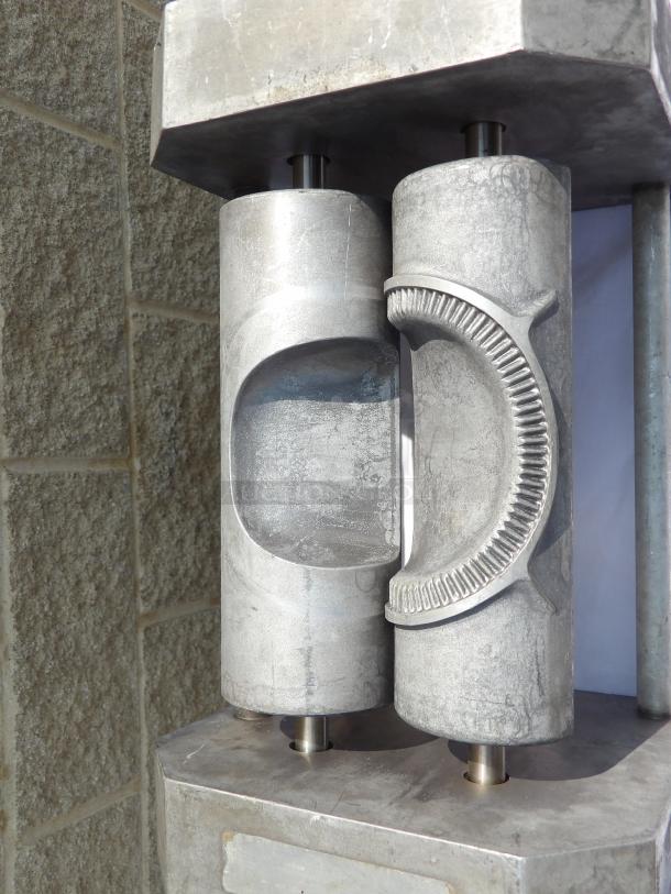 Metallic industrial machine component with cylindrical rollers and detailed grooves, used condition, no visible markings.