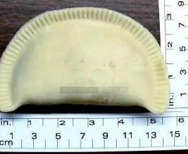 Cream-colored ceramic empanada sculpture, hand-sized, with ribbed edge detail, displayed on a metric and inch ruler grid.